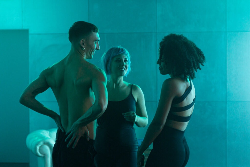 Three dancers in a blue room. The dancer in the middle is the singer PAENDA