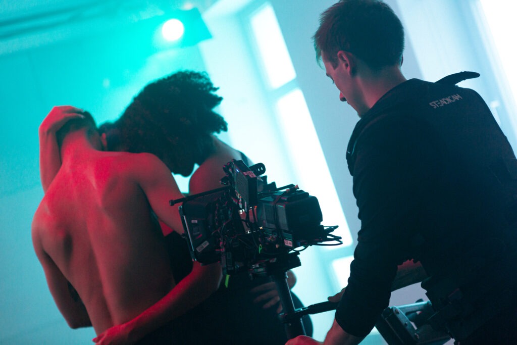 A film camera.in the background three dancers in a green, pink room