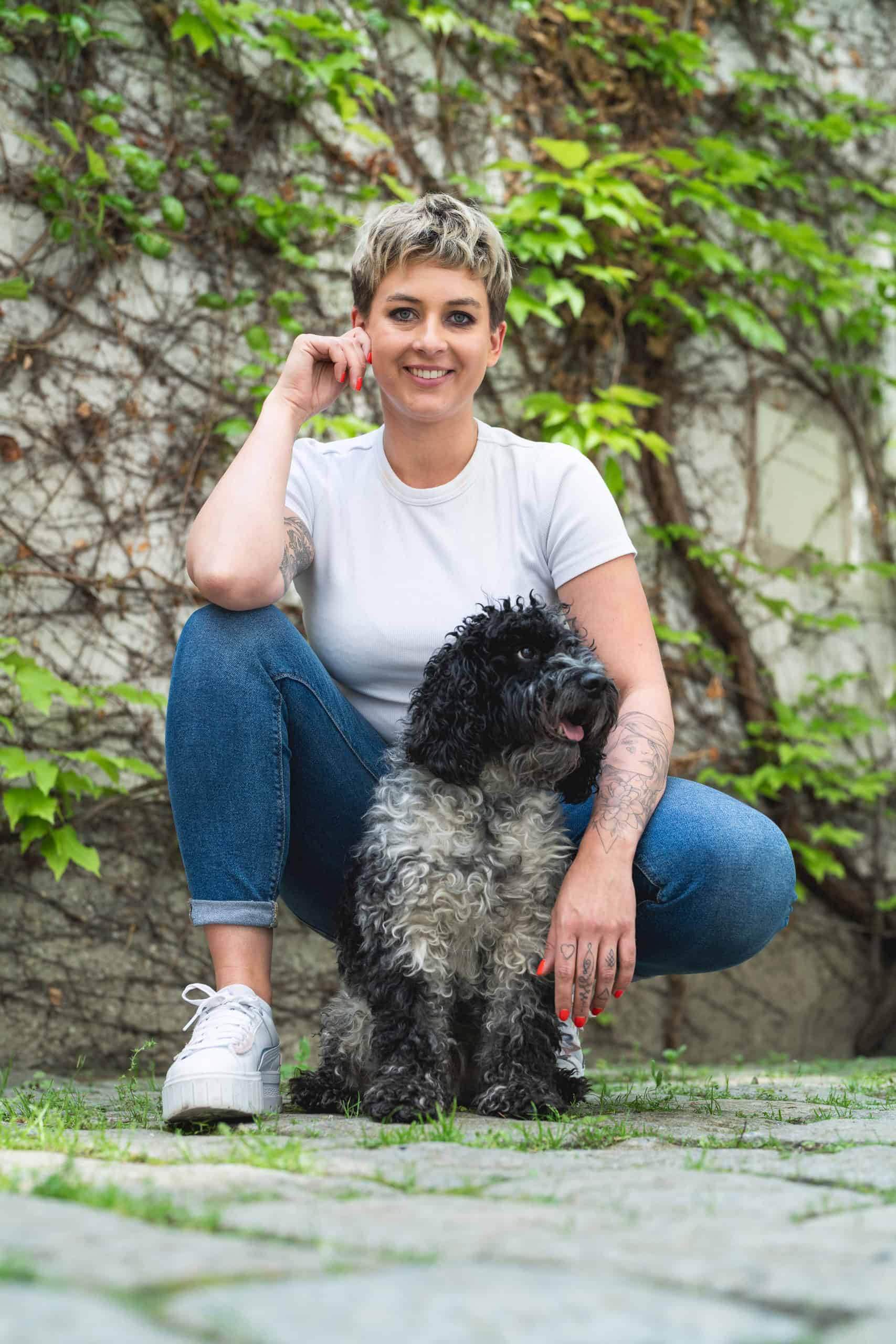 Portraitfoto_Paula_Lila_Mango_boxquadrat Paula Sidorczuk hocht am Boden mit ihrem Hund Mang vor einer grün bewachsenen Wand
