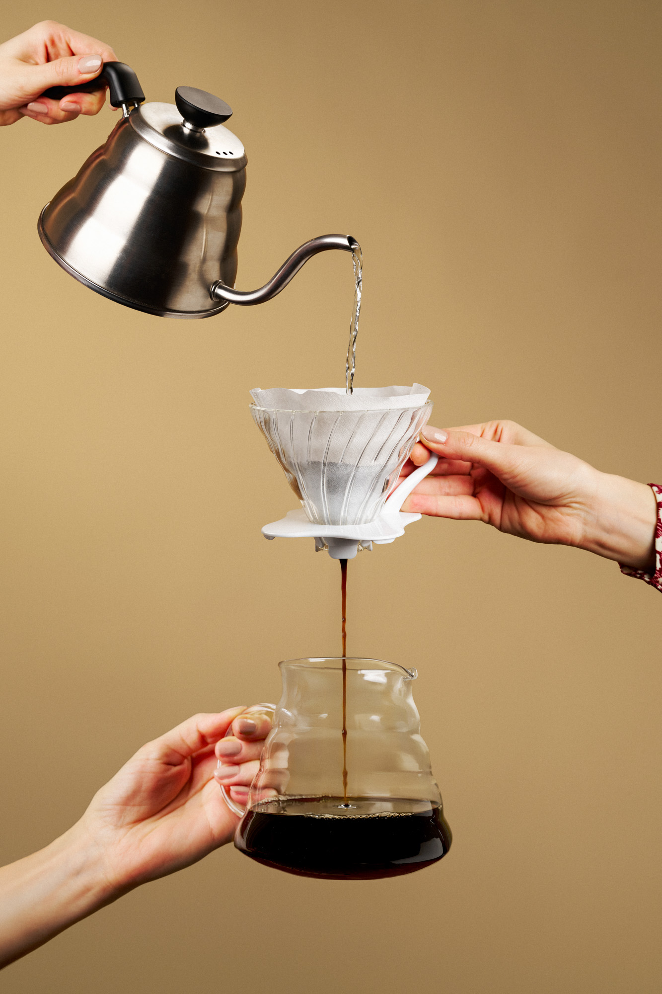boxquadrat_Julius_Meinl_Studio_Session Drei paar Hände halten untereinander je eine Wasserkanne einen kaffee Filter und eine Kaffee Karaffe. Oben fließt Wasser rein unten kommt Kaffee raus
