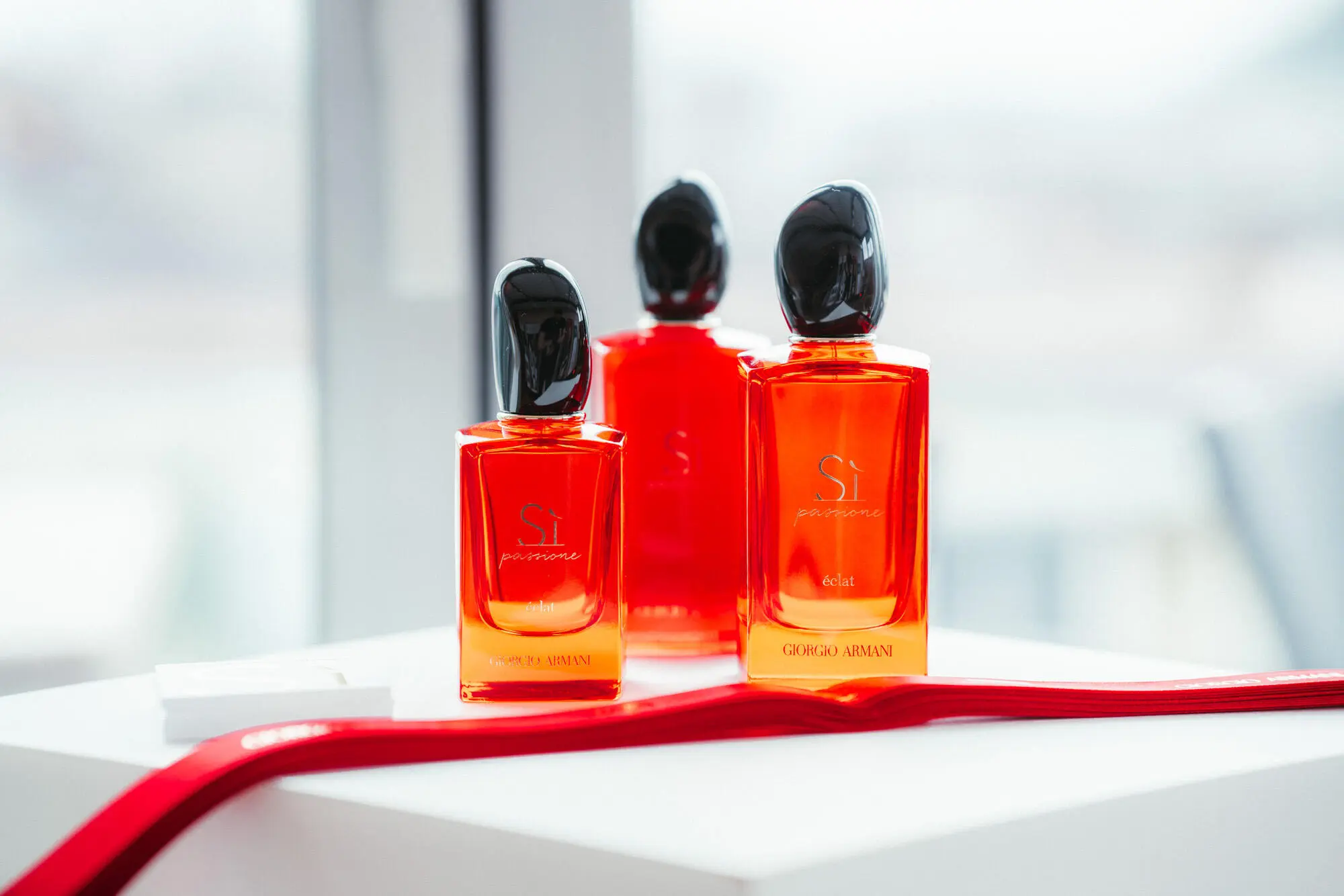 Produktfoto von drei roten Armani Parfum Flaschen auf weißem podest
