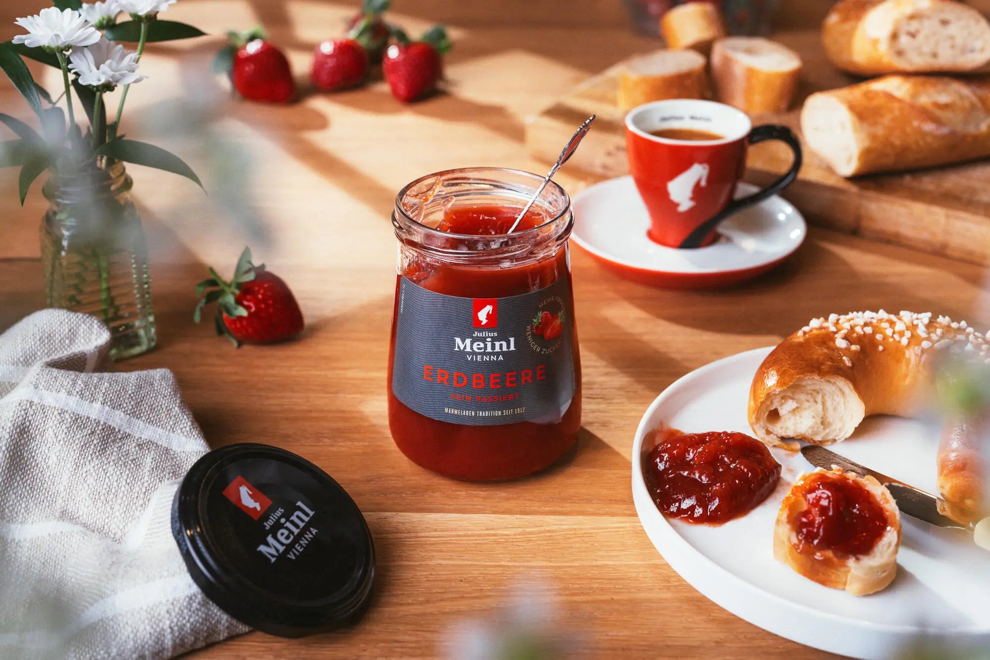 Produkfoto von einer offenen Julius Meinl Erdbeer Marmelade und einem abgebissenen Kipferl