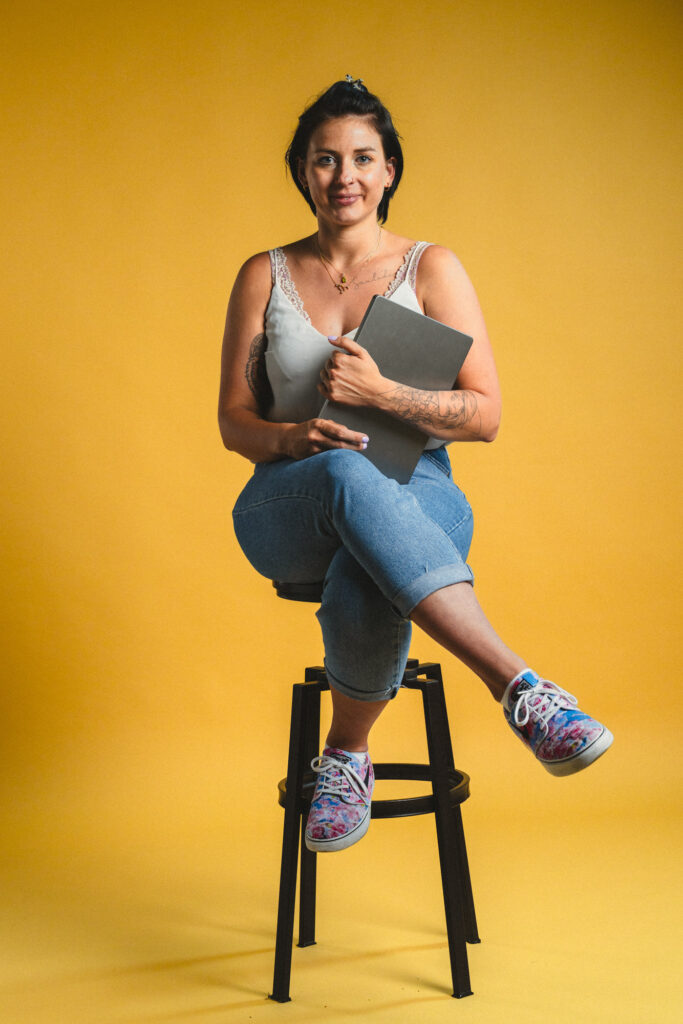 Ganzkörper Foto von Paula Sidorczuk, sitzend auf einem Hocker mit einem Laptop in der Hand, im boxquadrat Fotostudio 1160 Wien