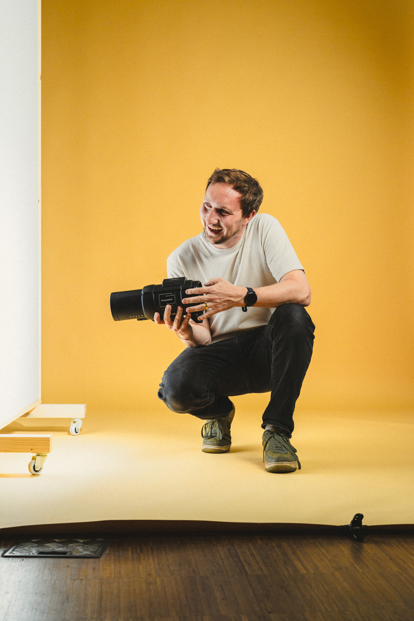 Ganzkörper Foto von Philipp Schulz, hockend am Boden mit Profoto Blitzkopf in der Hand, im boxquadrat Fotostudio 1160 Wien