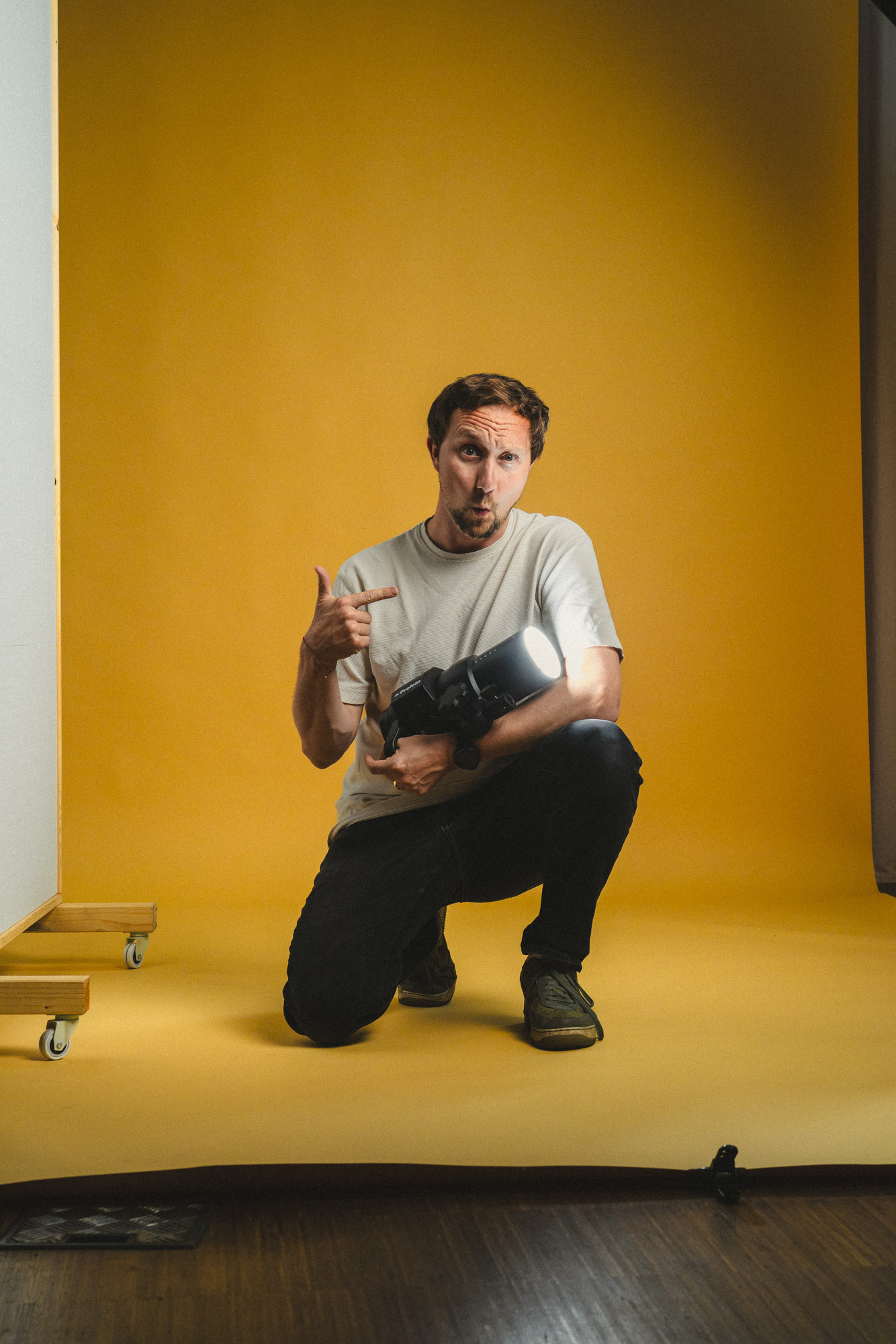 Ganzkörper Foto von Philipp Schulz, hockend am Boden mit Profoto Blitzkopf in der Hand, im boxquadrat Fotostudio 1160 Wien