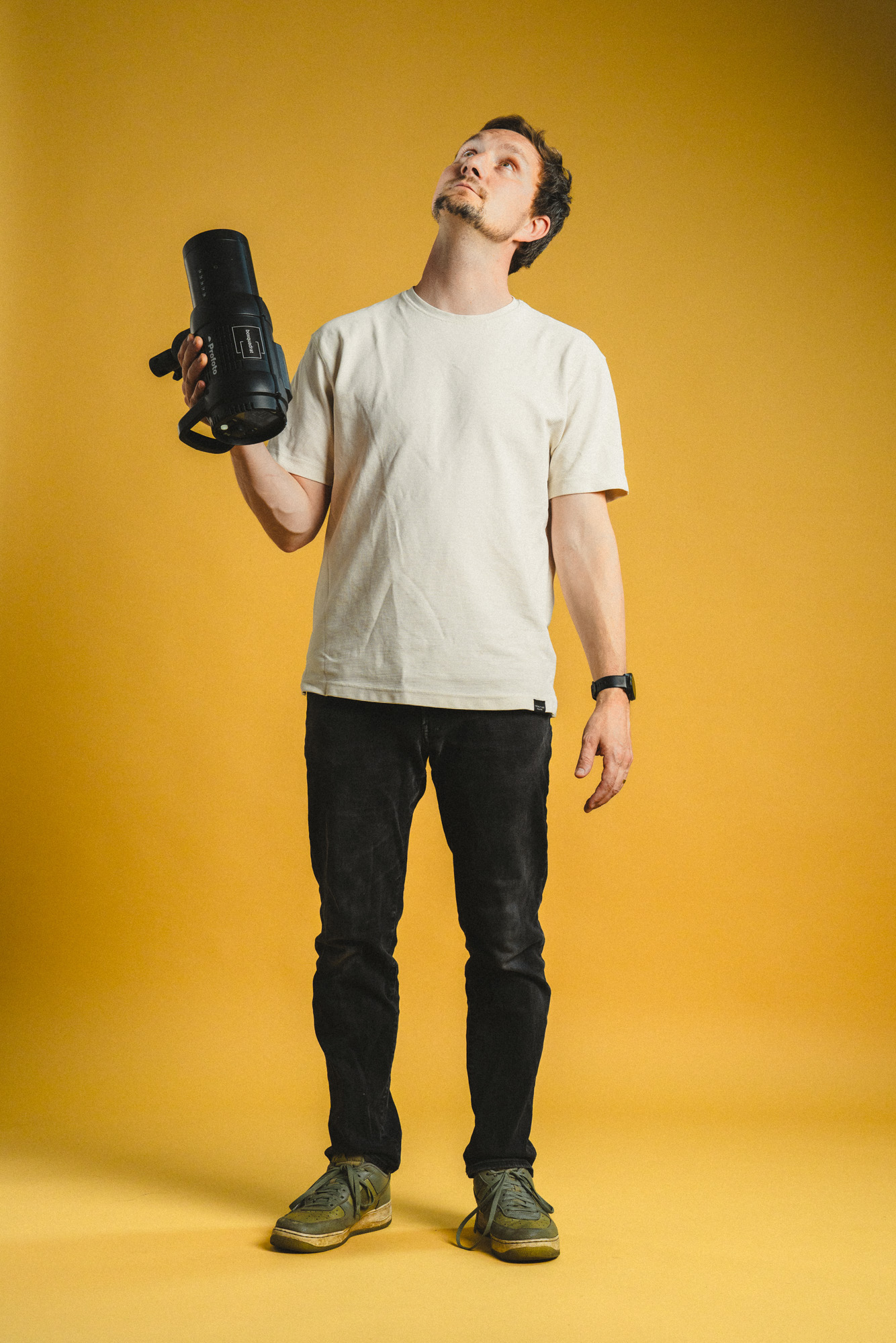 Ganzkörper Foto von Philipp Schulz, stehend und nach oben schauend mit Profoto Blitzkopf in der Hand, im boxquadrat Fotostudio 1160 Wien