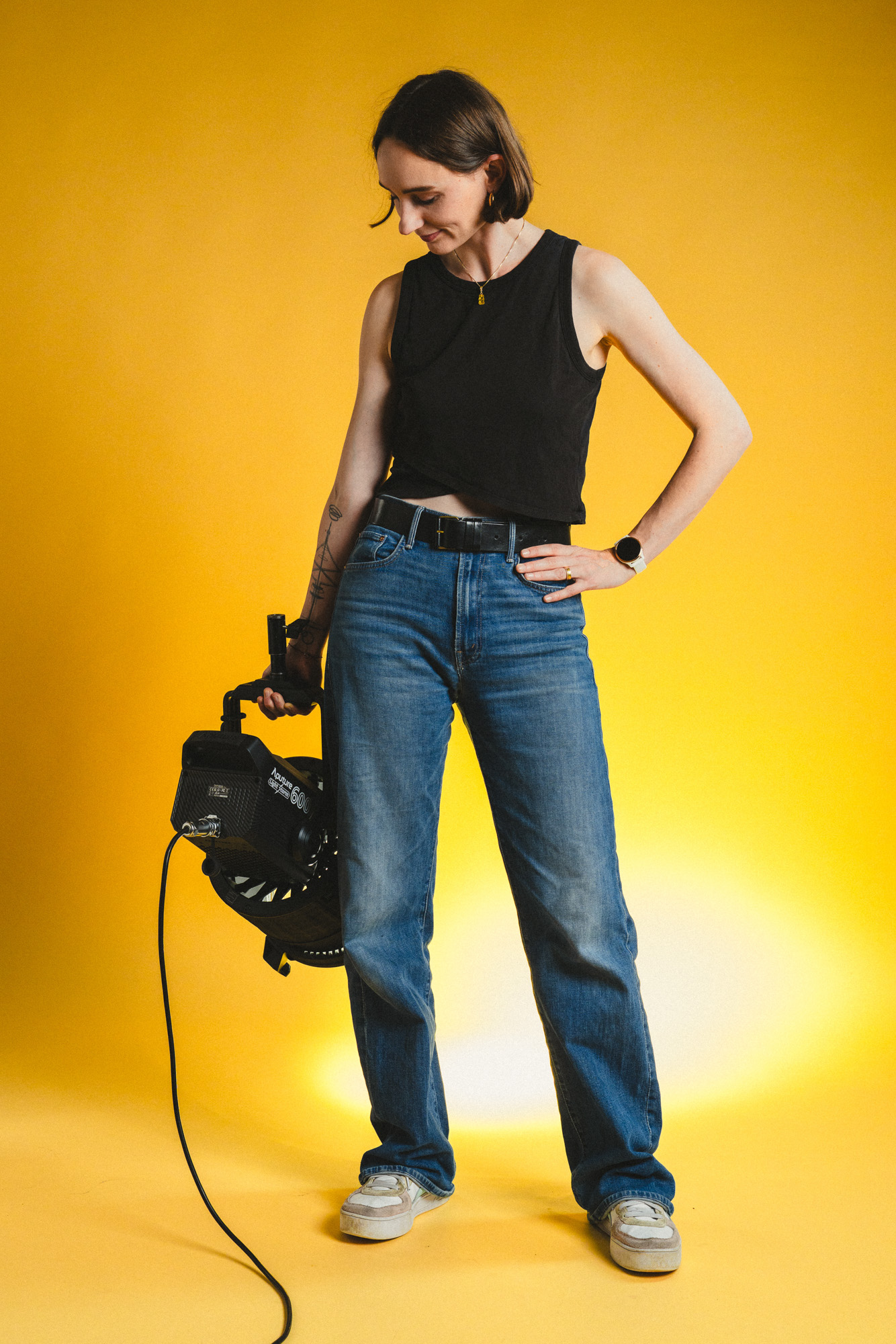 Ganzkörper Foto von Lauren Klocker, stehend mit Aputure 600x Licht in der Hand auf das Licht schauend, im boxquadrat Fotostudio 1160 Wien