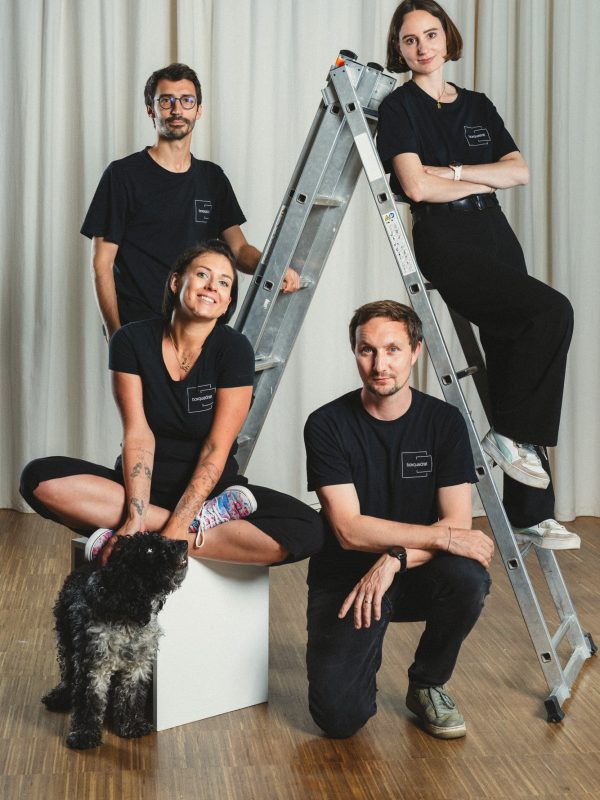 Studio und Content Agentur in Wien & Graz boxquadrat -Gruppenfoto mit Jakob Grill, Philipp Schulz, Paula Sidorczuk mit Hund Mango und Lauren Klocker auf einer silbernen Leiter im boxquadrat Fotostudio